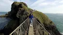 Seorang turis bersama anaknya melintasi Jembatan Carrick-a-Rede Rope di Pantai Causeway, Irlandia Utara, Rabu (8/4/2015). Jembatan tersebut diperkirakan telah dibangun selama lebih dari 350 tahun oleh para nelayan salmon. (REUTERS/Cathal McNaughton) 