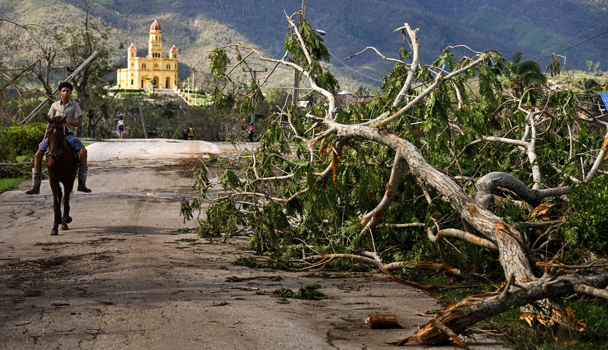 Seorang warga berkuda melewati pohon tumbang, kabel listrik, dan rumah-rumah yang hancur setelah Badai Melissa melanda El Cobre, Provinsi Santiago de Cuba, Kuba pada Kamis 30 Oktober 2025. Pemerintah Kuba telah mengeluarkan peringatan badai untuk lima provinsi, yaitu Granma, Santiago de Cuba, Guantanamo, Holguin, dan Las Tunas. (YAMIL LAGE/AFP)