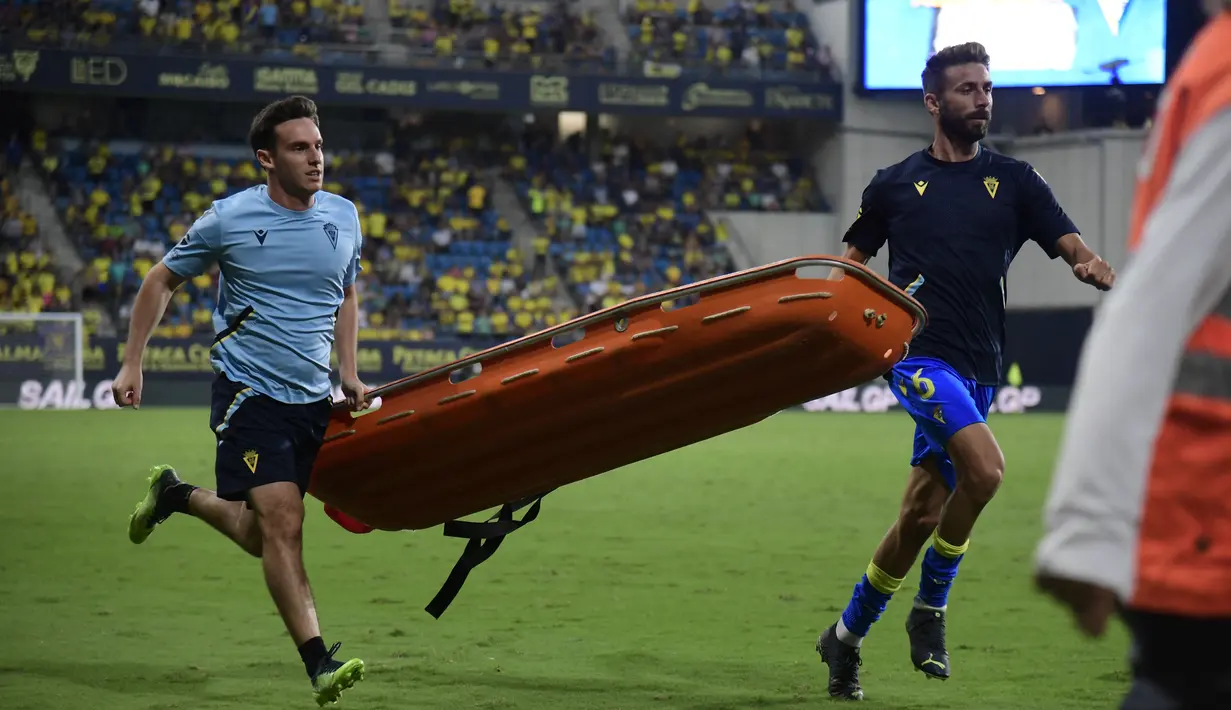 Petugas ofisial dari Cadiz juga sigap membawakan tandu untuk diberikan kepada petugas medis agar suporter yang mengalami insiden darurat medis bisa dibawa keluar stadion dan diberikan penanganan yang cepat. (AFP/Cristina Quicler)