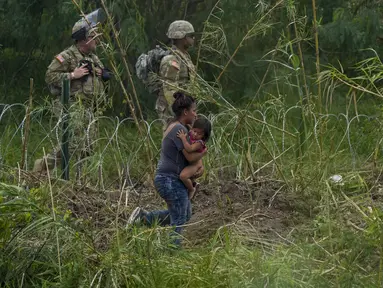 Petugas Garda Nasional Texas berdiri di sepanjang bentangan kawat berduri saat migran perempuan yang membawa seorang anak mencoba menyeberang ke AS, di tepi Rio Grande, seperti yang terlihat dari Matamoros, Meksiko, Kamis (11/5/2023). (AP Photo/Fernando Llano)