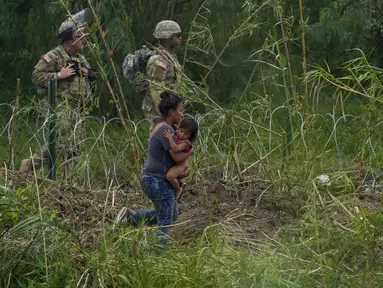 Petugas Garda Nasional Texas berdiri di sepanjang bentangan kawat berduri saat migran perempuan yang membawa seorang anak mencoba menyeberang ke AS, di tepi Rio Grande, seperti yang terlihat dari Matamoros, Meksiko, Kamis (11/5/2023). (AP Photo/Fernando Llano)