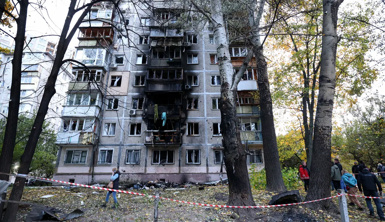 Penduduk setempat berjalan di sekitar gedung bertingkat mereka yang rusak akibat ledakan serangan pesawat tak berawak di Kyiv, pada 30 Oktober 2024. (Anatolii STEPANOV/AFP)