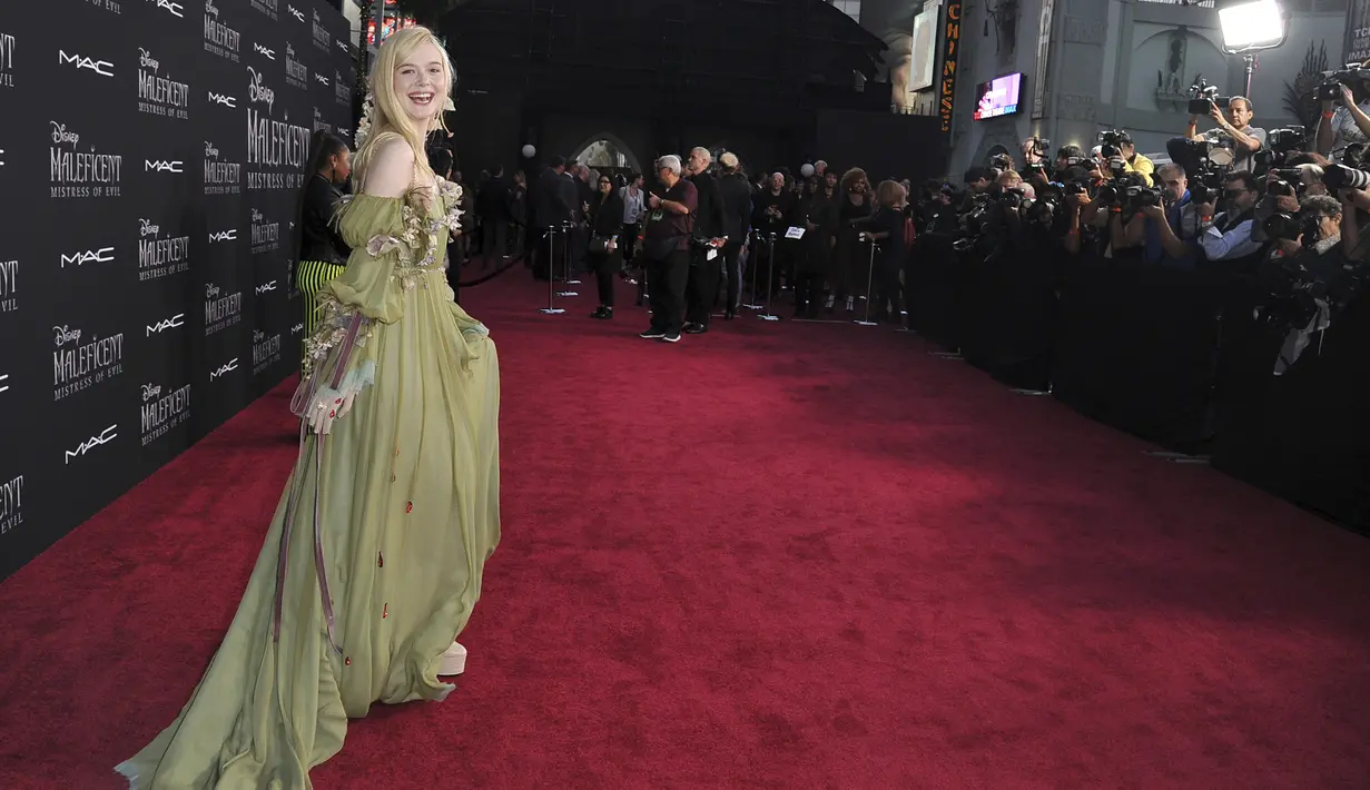 Elle Fanning tertawa di karpet merah pemutaran perdana film Disney "Maleficent: Mistress of Evil" di Teater El Capitan di Hollywood (30/9/2019). Elle Fanning tampil bergaun hijau dengan sarung tangan tipis dann tetesan darah merah berhiaskan permata di tangan kanannya. (AP Photo/Richard Shotwell)