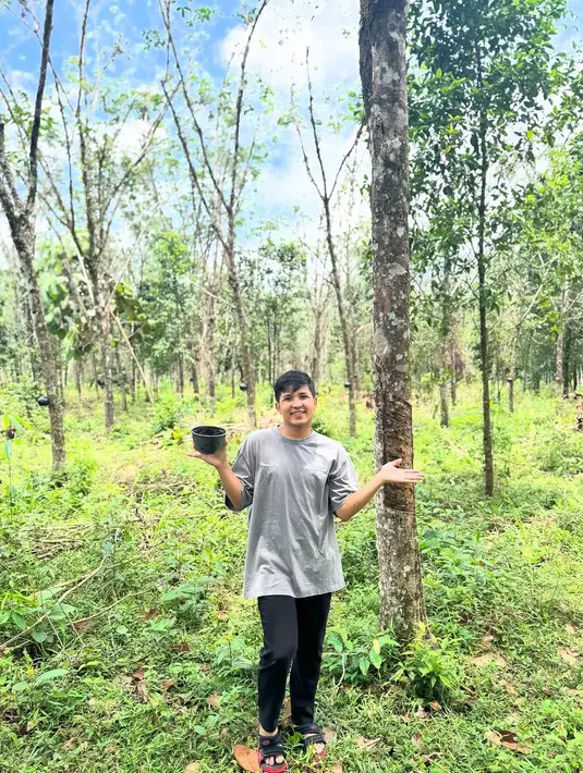 Dalam salah satu video, Jirayut juga membagikan suasana di area kebun. Jirayut berdiri di kebun karetnya yang luas. Latar belakang memperlihatkan puluhan pohon karet yang berjajar rapi. Langit yang cerah dan rumput hijau menambah kesan natural dan tenang.   (Liputan6.com/IG/@jirayutdaa4official)