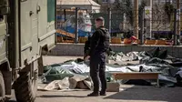 Seorang polisi Ukraina berdiri di dekat mayat yang ditutupi lembaran plastik setelah serangan roket yang digunakan untuk evakuasi sipil di sebuah stasiun kereta api di Kramatorsk, Ukraina timur (8/4/2022). (AFP/Fadel Senna)