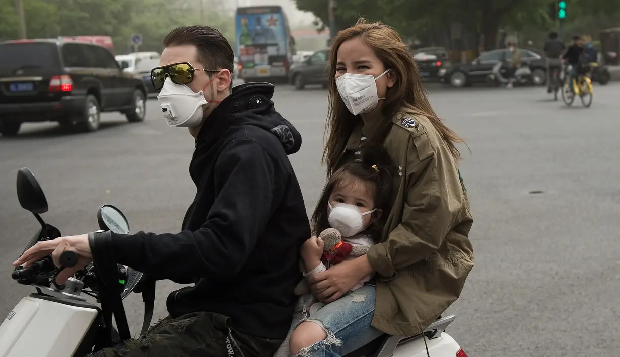 Sebuah keluarga mengendarai motor sambil mengenakan masker saat badai debu menerjang kota Beijing, China, Kamis (4/5). Imbas dari badai tersebut, jarak pandang di Beijing turun drastis hingga satu kilometer, di pagi hari. (Nicolas ASFOURI/AFP)