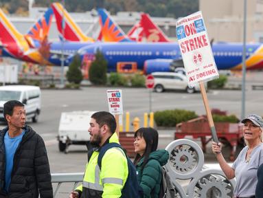 Orang-orang membawa tanda-tanda pemogokan Boeing saat mereka berjalan melewati pesawat Boeing 737 yang diparkir di dekat Boeing Field setelah aksi mogok kerja untuk Asosiasi Mekanik dan Pekerja Kedirgantaraan Internasional (IAM) di Seattle Union Hall di Seattle, Washington, pada tanggal 15 Oktober 2024. (Jason Redmond/AFP)