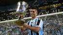 Pemain Gremio, Luis Suarez mengangkat trofi setelah memenangkan Gaucho Championship di Arena do Gremio Stadium, Porto Alegre, Brasil, 8 April 2023. Suarez menjadi pencetak gol penentu kemenangan ke gawang Caxias pada laga leg kedua final. (AFP/Silvio Avila)