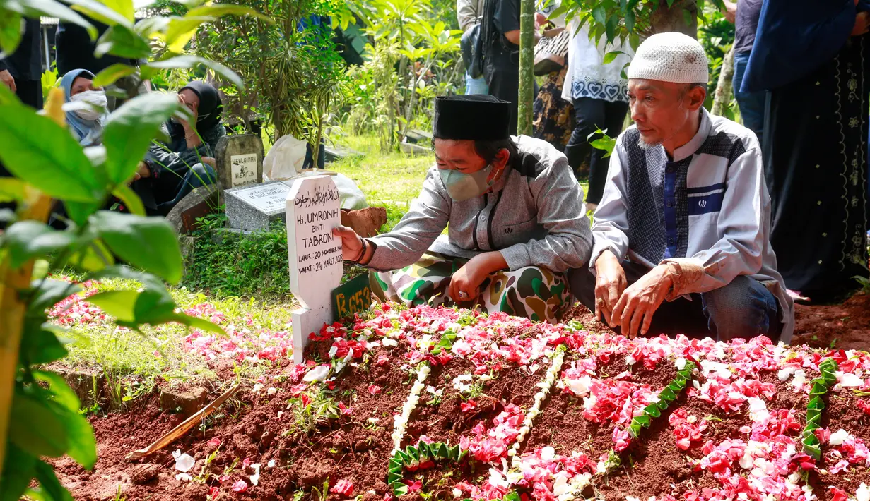 Kesedihan Adul saat di atas pusara makan sang ibunda. Meski mengenakan masker, tapi begitu jelas gurat kesedihannya. Memegang papan nisan sang ibunda. Adul mengenakan gamis abu-abu dengan sarung loreng  hijau dan mengenakan peci hitam. [Foto: Muhammad Akrom Sukarya/© KapanLagi.com]