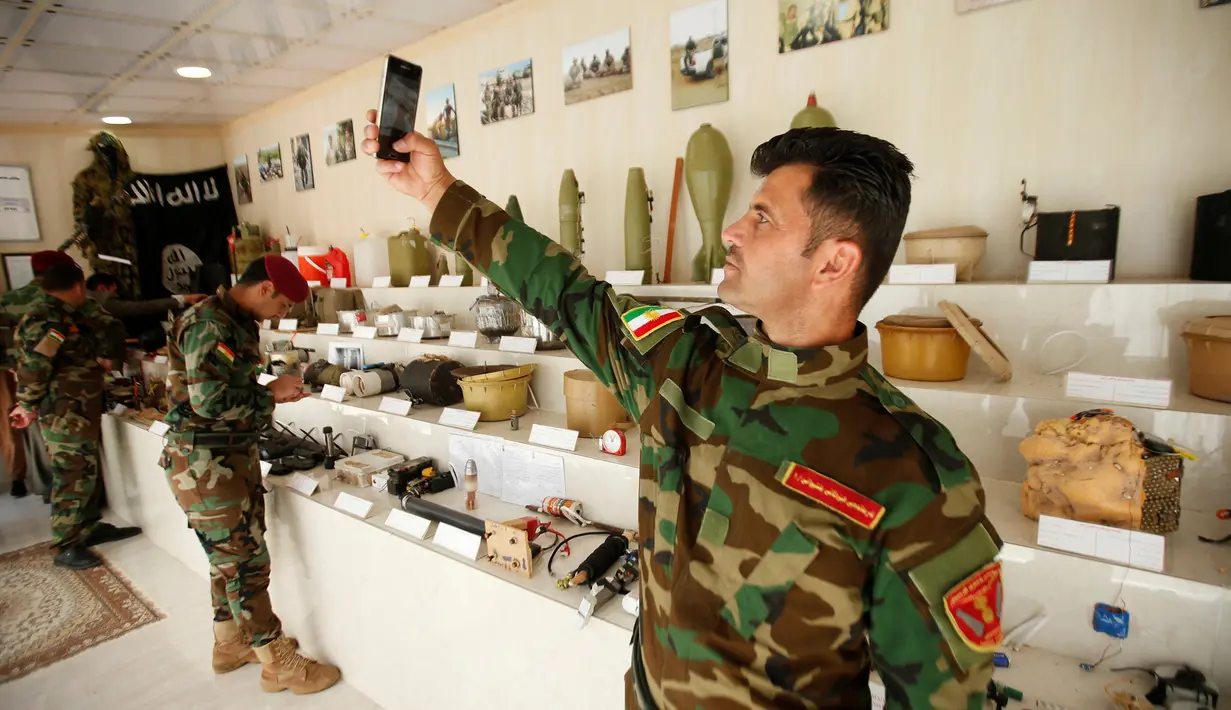 Seorang militer Kurdi Peshmerga berswafoto di sebelah bahan peledak dan barang-barang yang digunakan oleh militan Negara Islam (ISIS) di sebuah museum di Erbil, Irak, 12 Mei 2019. 'Museum ISIS' tersebut dibuka oleh militer Peshmerga. (REUTERS/Azad Lashkari)