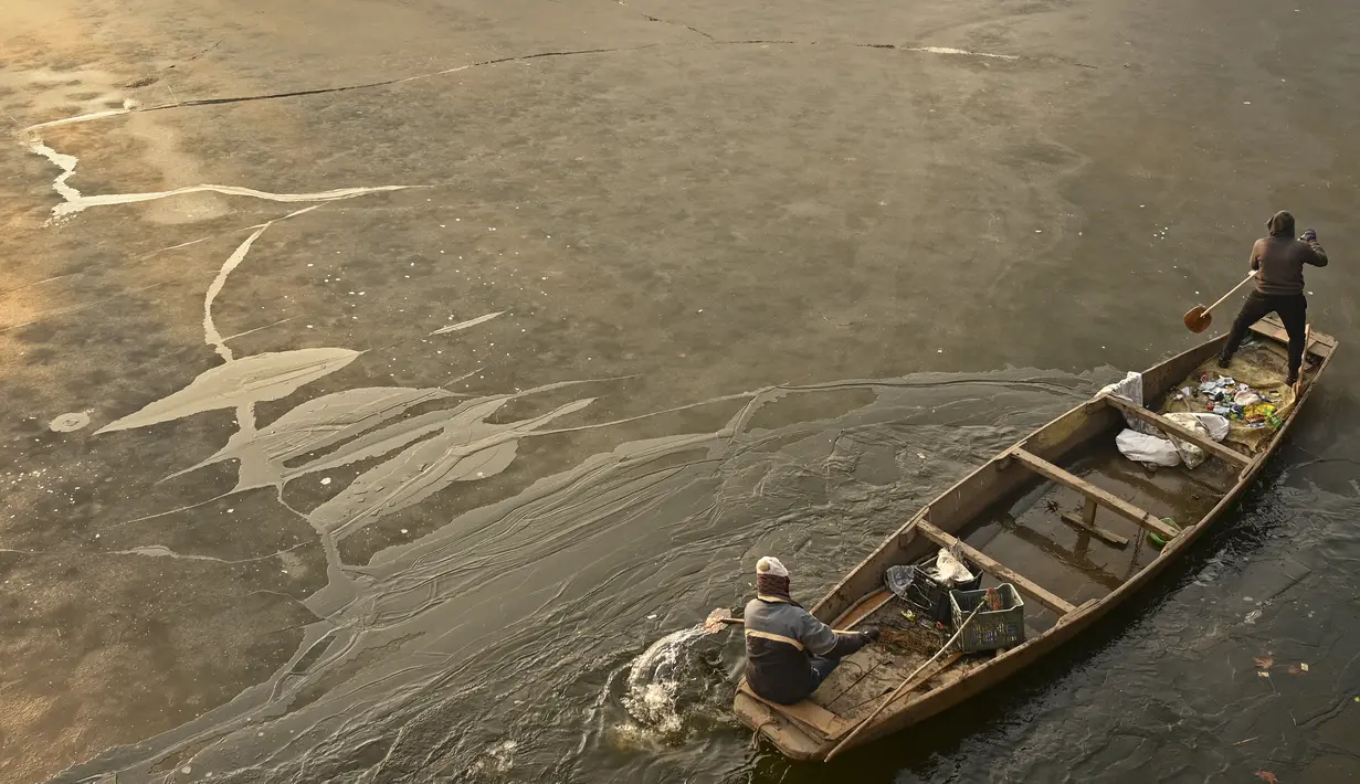 Tukang perahu menggunakan dayung memecahkan lapisan es di sepanjang bagian dalam Danau Dal pada pagi saat musim dingin di Srinagar (2/1/2023). Periode musim dingin yang keras selama 40 hari yang dikenal sebagai 'Chillai Kalan' memperketat cengkeramannya di Kashmir pada hari Senin karena suhu malam semakin turun. (AFP/Tauseef Mustafa)