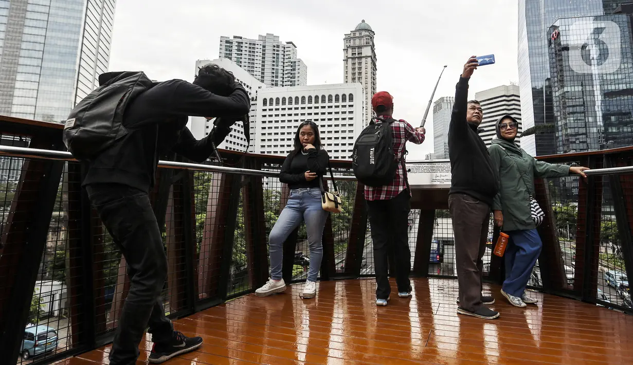 Warga berswafoto dengan kamera ponsel di Jembatan Penyeberangan Orang (JPO) Pinisi, Jalan Jenderal Sudirman, Karet, Jakarta, Selasa (15/3/2022). Belum lama ini, Pemprov DKI Jakarta meresmikan JPO berbentuk spesial tersebut yang membentang di atas Jalan Jenderal Sudirman. (Liputan6.com/Johan Tallo)