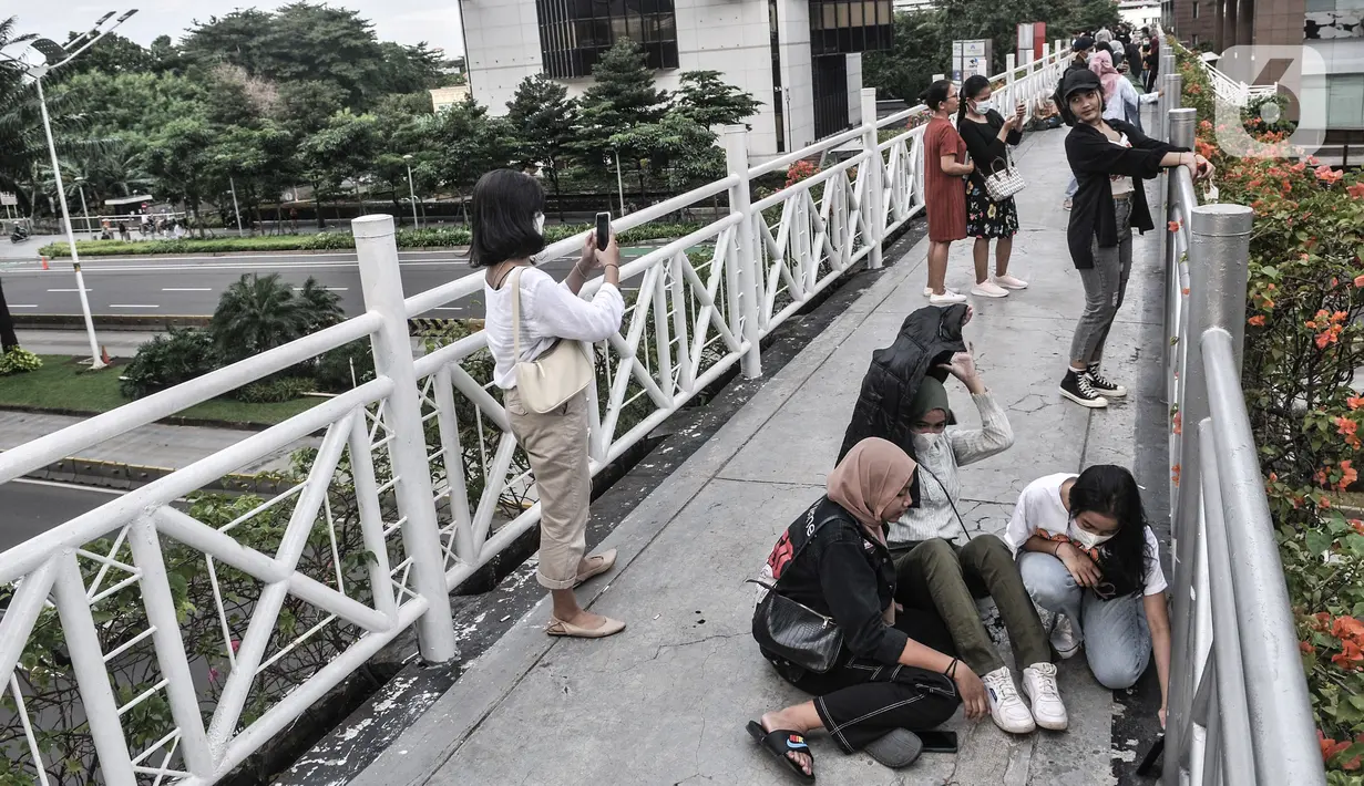 Warga berfoto di jembatan penyeberangan orang (JPO) tanpa atap di kawasan Sudirman, Jakarta, Minggu (4/4/2021). JPO tanpa atap masih menjadi wisata alternatif warga ibu kota dalam menghabiskan waktu akhir pekan untuk berfoto-foto dengan latar belakang gedung perkantoran (merdeka.com/Iqbal S Nugorho