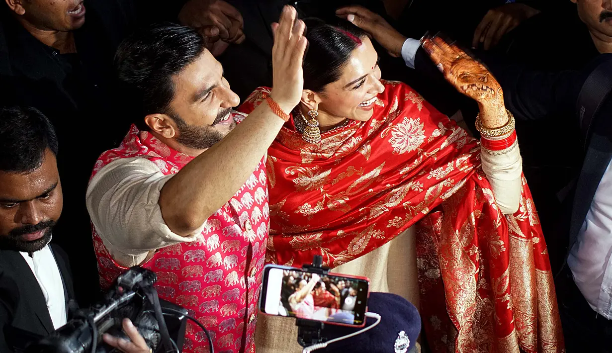 Pasangan pengantin baru, Ranveer Singh dan Deepika Padukone menyapa penggemar yang menyambut mereka di bandara internasional Mumbai, Minggu (18/11). Pasangan bintang Bollywood India itu baru saja kembali dari acara pernikahan mereka di Italia. (AFP)