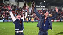 Aktor Hollywood, Ryan Reynolds (kanan) dan pemilik klub Wrexham, Rob McElhenney merayakan kesuksesan dengan mengangkat trofi setelah klub mereka berhasil promosi ke Liga Dua Inggris. Wrexham menang atas Boreham Wood dengan skor 3-1 pada laga English National League di Racecourse Ground Stadium, Wrexham, Wales, Sabtu (22/04/2023). (AFP/Oli Scarff)