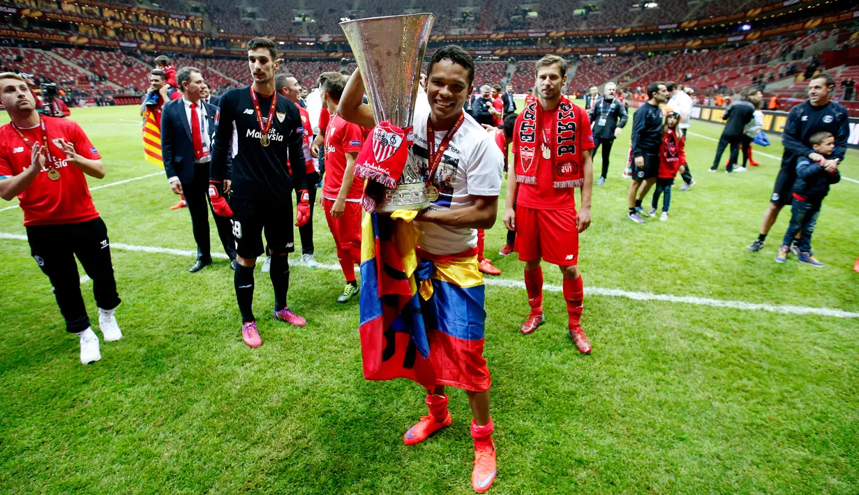 Carlos Bacca memperlihatkan trofi ke pendukung setia Sevilla di tengah perayaan gelar Liga Europa 2015 di Stadion Narodowy, Polandia, Kamis (28/5/2015). Sevilla memecahkan rekor meraih trofi Liga Europa terbanyak, yakni empat gelar. (Reuters/Carl Recine)