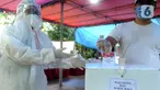 Petugas Kelompok Penyelenggara Pemungutan Suara (KPPS) dengan memakai baju hazmat membantu pemilih memasukkan kertas suara usai menggunakan hak pilihnya dalam Pilkada Tangerang Selatan 2020 di TPS 46, Paku Jaya, Serpong Utara, Rabu (9/12/2020). (merdeka.com/Arie Basuki)