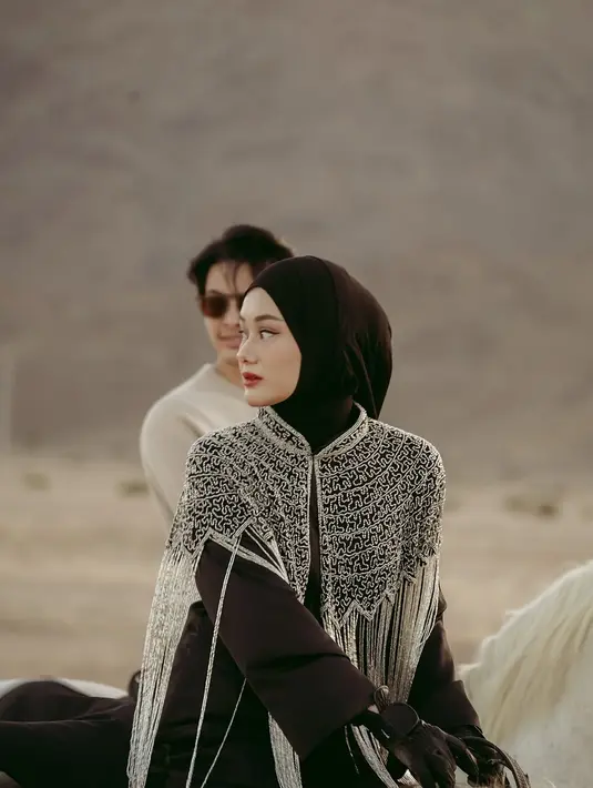 Outfit Dinda Hauw sangat cocok dengan suasana gurun pasir yang dramatis, memberikan nuansa Timur Tengah yang kental. Karena itu, banyak netizen menyebutnya mirip warga lokal Madinah. Kepercayaan dirinya saat menunggang kuda juga patut diacungi jempol. (Liputan6.com/IG/@rey_mbayang)