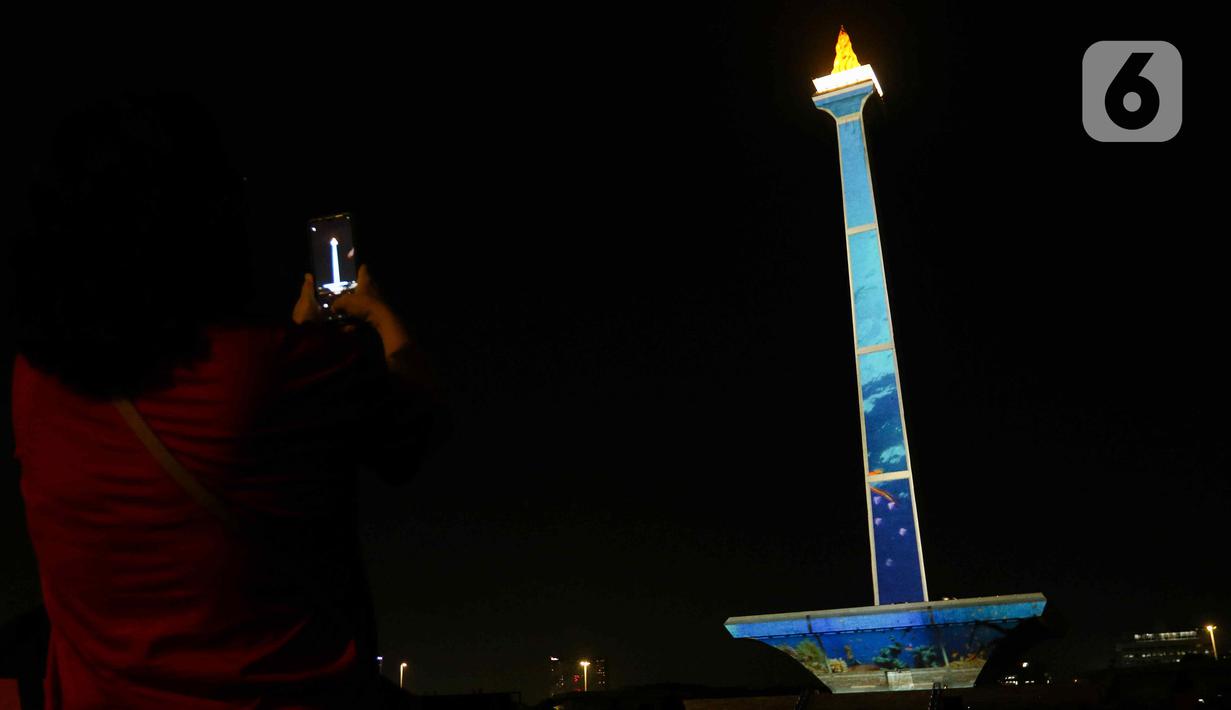 Pengunjung mengambil gambar video mapping dalam Monas Week 2023 di tugu Monumen Nasional (Monas), Jakarta Pusat, Jumat (29/12/2023). (Liputan6.com/Herman Zakharia)