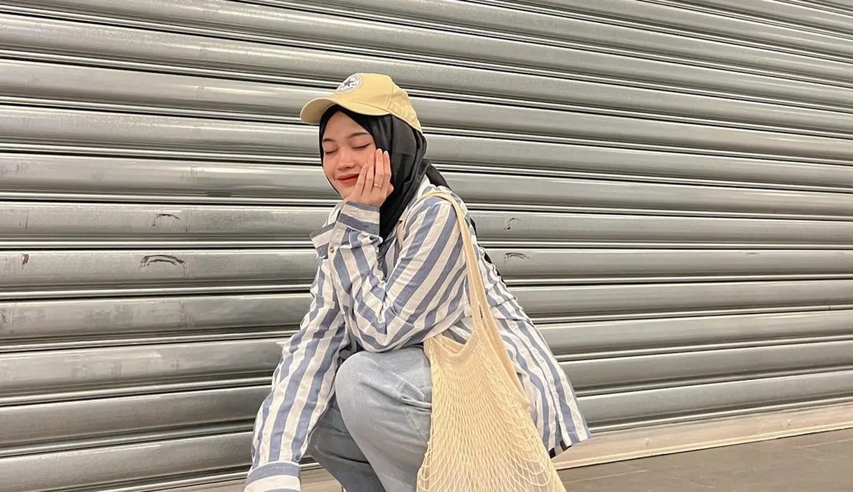 Kombinasi striped shirt dengan celana jeans, hijab, dan topi baseball nyaman dan stylish untuk hangout. [Foto: IG/putridelinaa].