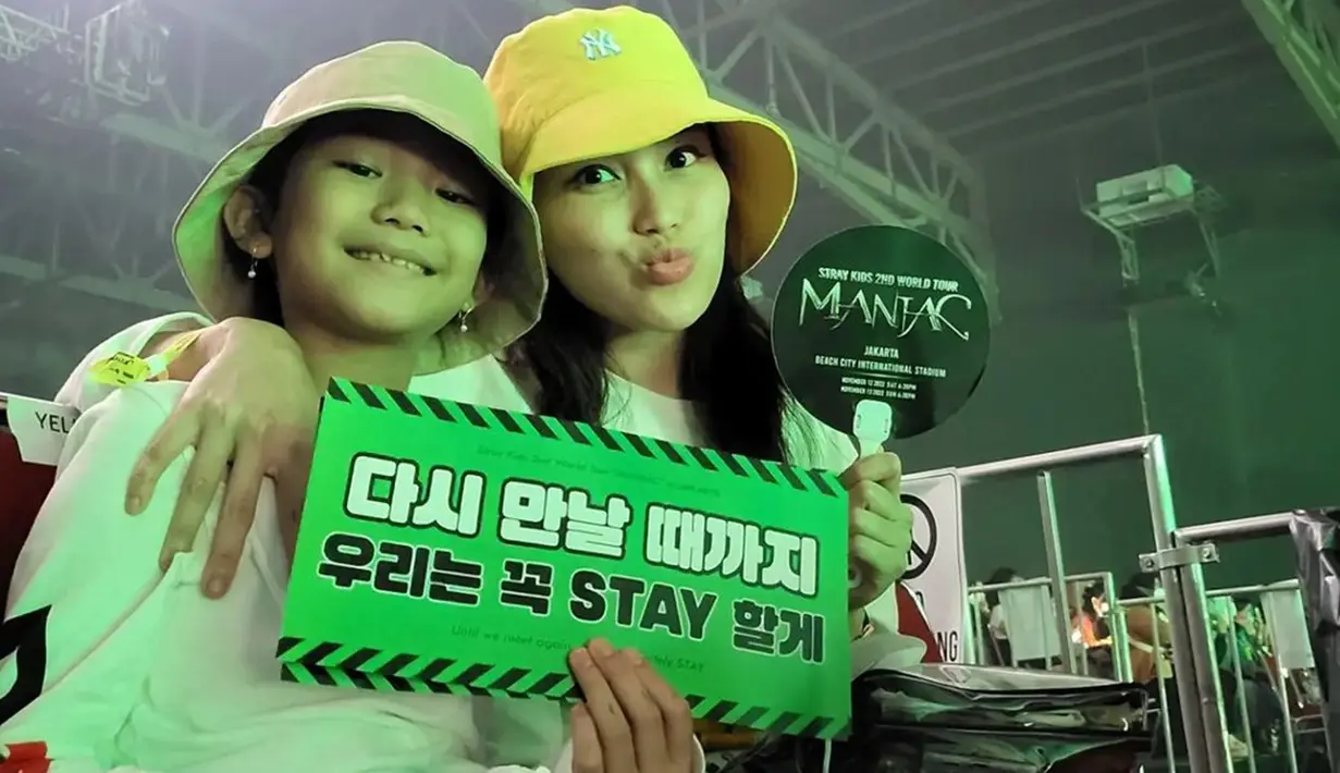 Ibu dan anak satu ini pun tampil kompak dengan kaos putih serta bucket hat. Keduanya juga turut memegang hand banner sebagai penggemar Stray Kids, STAY. (Liputan6.com/IG/@ayutingting92)