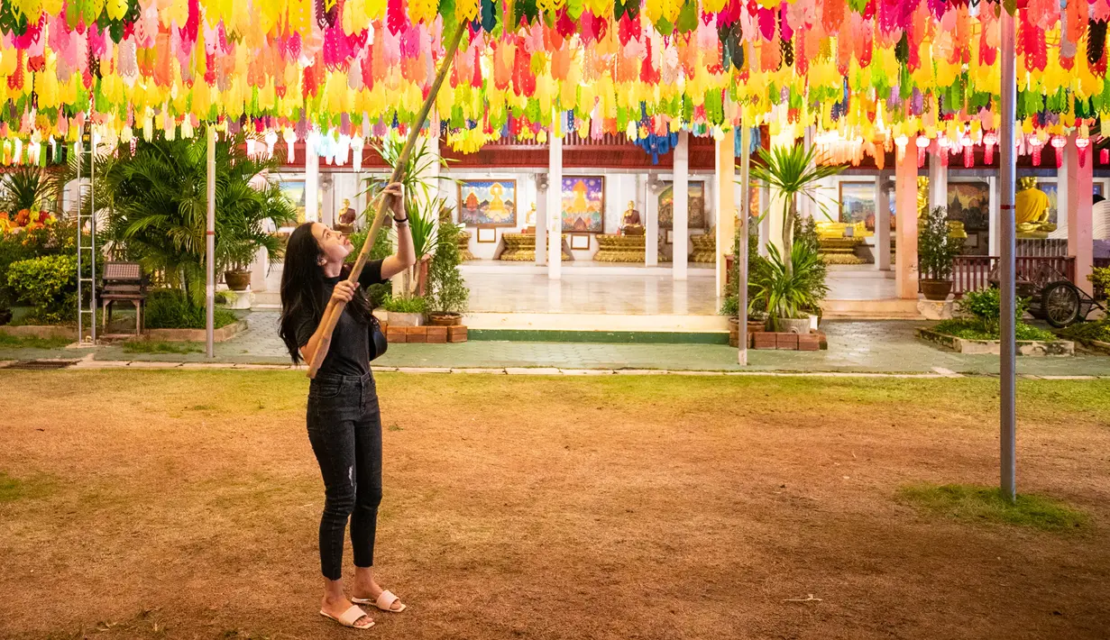 Seorang perempuan menggantung lampion di Wat Phra That Hariphunchai, Lamphun, Thailand, 1 November 2020. Sekitar 100.000 lampion digantung di Wat Phra That Hariphunchai sebagai bagian dari perayaan festival tradisional Yi Peng. (Xinhua/Zhang Keren)