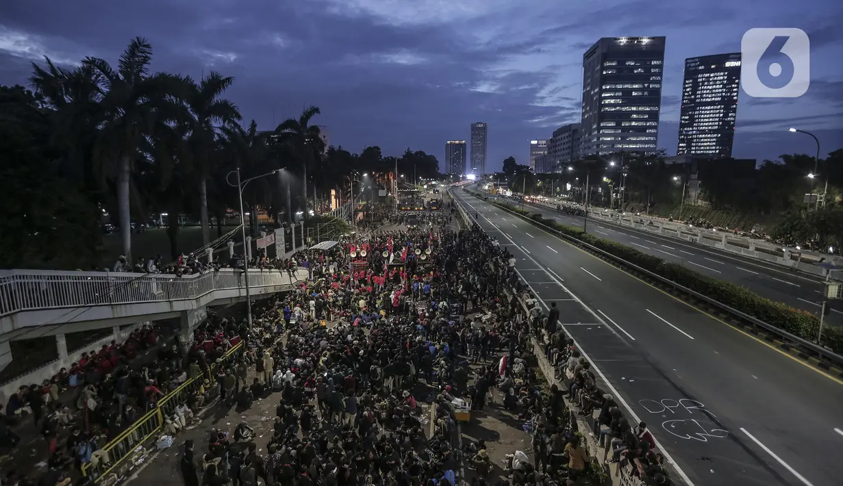 Mahasiswa dan elemen buruh bertahan hingga malam saat aksi di depan Gedung DPR/MPR/DPD, Jakarta, Kamis (16/7/2020). Dalam aksinya, mereka menolak pengesahan RUU Cipta Kerja atau Omnibus Law yang saat ini sedang dibahas DPR bersama pemerintah. (Liputan6.com/Johan Tallo)
