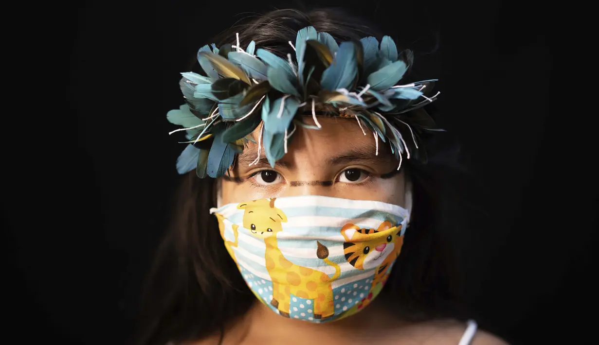 Iasmin (8) dari kelompok etnis pribumi Sateré Mawé mengenakan pakaian tradisional sukunya dan masker saat pandemi virus corona COVID-19 di Manaus, Brasil, Rabu (27/5/2020). (AP Photo/Felipe Dana)