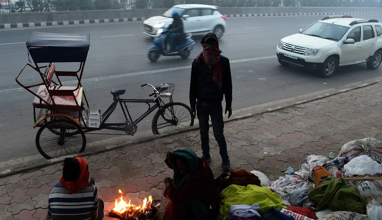 Para tunawisma menghangatkan diri dengan api kecil di pagi berkabut dingin di New Delhi (25/12). India ditetapkan darurat polusi udara. Kualitas udara yang semakin buruk dan kabut beracun menyelimuti. (AFP Photo/Prakash Singh)