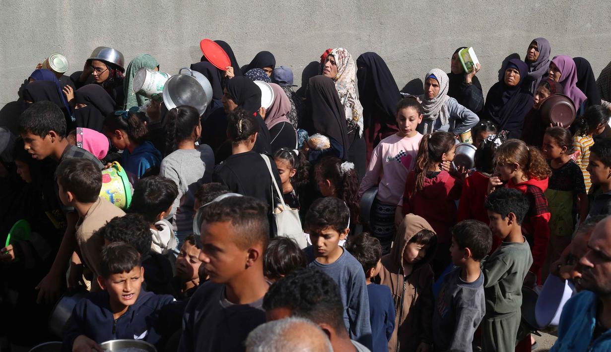 PBB juga melaporkan bahwa lebih dari 100 permintaan misi bantuan ke Gaza telah ditolak oleh Israel sejak gencatan senjata dimulai. Tampak dalam foto, warga Palestina yang terlantar, anak-anak, dan dewasa, menunggu makanan di sebuah tempat penampungan yang telah dihuni keluarga-keluarga di Nuseirat, pusat Jalur Gaza, pada 23 November 2025. (EYAD BABA/AFP)