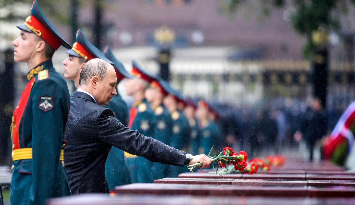 Presiden Rusia, Vladimir Putin meletakkan bunga di tengah hujan lebat saat upacara kehormatan untuk memperingati invasi Nazi Jerman pada 1941 di Benteng Kremlin, Moskow, Kamis (22/6). (Alexei Druzhinin/Sputnik, Kremlin Pool Photo via AP)