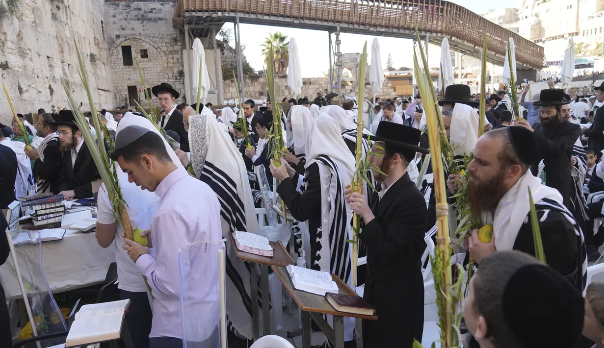 Para penyembah mengadakan empat spesies Sukkot berkumpul untuk diberkati oleh pria Yahudi ultra-Ortodoks dari kasta Imam Cohanim berdoa tertutup selendang doa selama hari raya Yahudi Sukkot di Tembok Barat, situs paling suci di mana orang Yahudi dapat berdoa, di Kota Tua Yerusalem Rabu, 12 Oktober 2022. (AP Photo/Tsafrir Abayov)