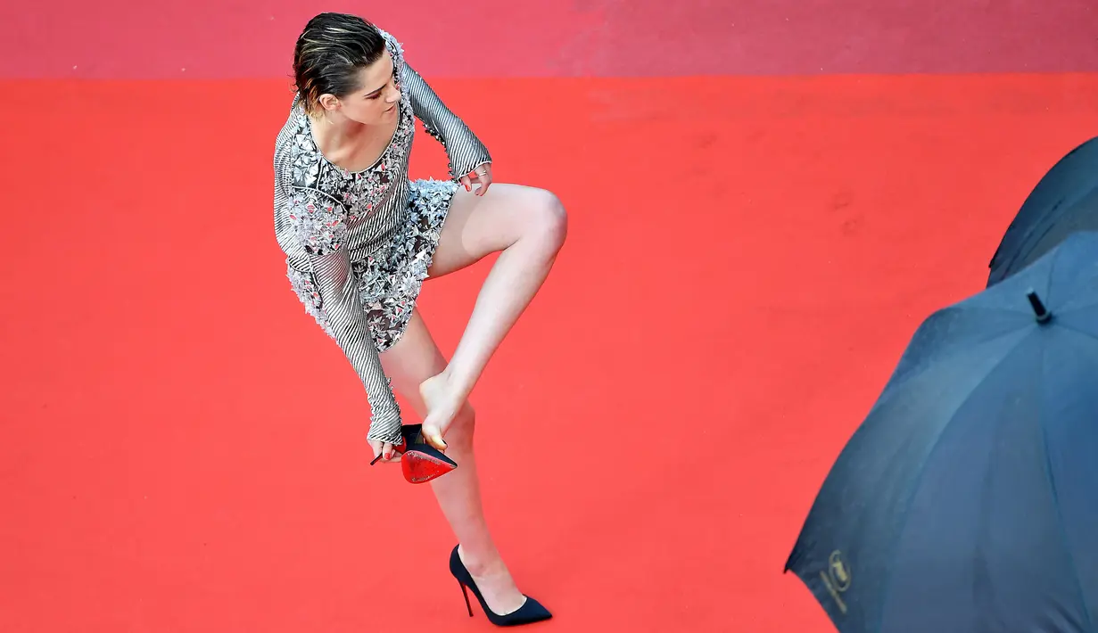 Kristen Stewart melepas sepatunya setelah berpose di karpet merah pemutaran film BlackKkKlansman pada Festival Film Cannes, Prancis, Senin (14/5). Kristen Stewart mencopot high heels hitamnya saat menaiki tangga menuju arena teater. (AFP/Alberto PIZZOLI)