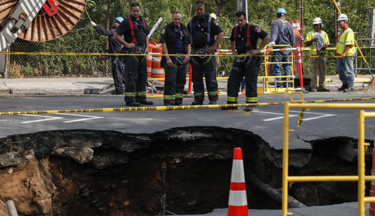 Petugas pemadam kebakaran mengamati  lubang besar (sinkhole) di wilayah Brooklyn, New York, Selasa (4/8/2015). Lubang yang terbentuk di persimpangan pemukiman Sunset Park itu disebabkan erosi dan merusak pipa air serta aspal jalan. (AFP/Kena Betancur)