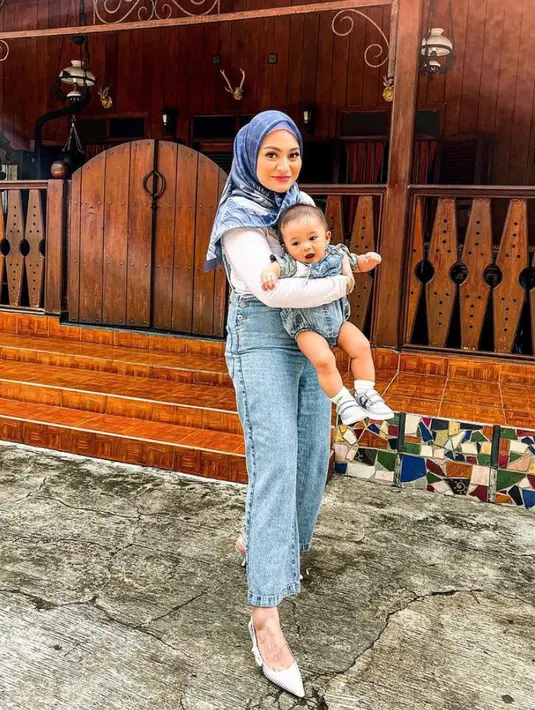 2. Nathalie kompak bersama baby Adzam mengenakan baju overall jeans dan inner warna putih. Gayanya dipadukan dengan hijab bermotif warna biru senada. (Instagram/nathalieholscher).