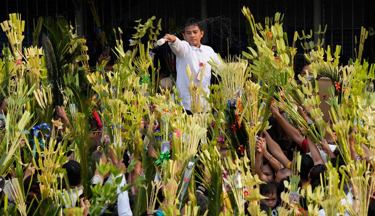Pada hari ini, Minggu 29 Maret 2026, umat Kristiani beramai-ramai membawa daun palem untuk diberkati ke gereja sebagai simbol penghormatan dan kemenangan, menyambut Yesus sebagai Raja dalam kehidupan sehari-hari. Tampak dalam foto, seorang pekerja gereja memercikkan air suci ke daun palem para umat selama upacara pemberkatan di luar Katedral Antipolo, kota Antipolo, provinsi Rizal, Filipina, saat memperingati Minggu Palma, 29 Maret 2026. (AP Photo/Aaron Favila)