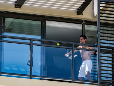 Petenis pria peringkat satu dunia, Novak Djokovic melakukan latihan di balkon hotel, Adelaide, Australia, Rabu (20/1/2021). (Foto: AFP/Morgan Sette)