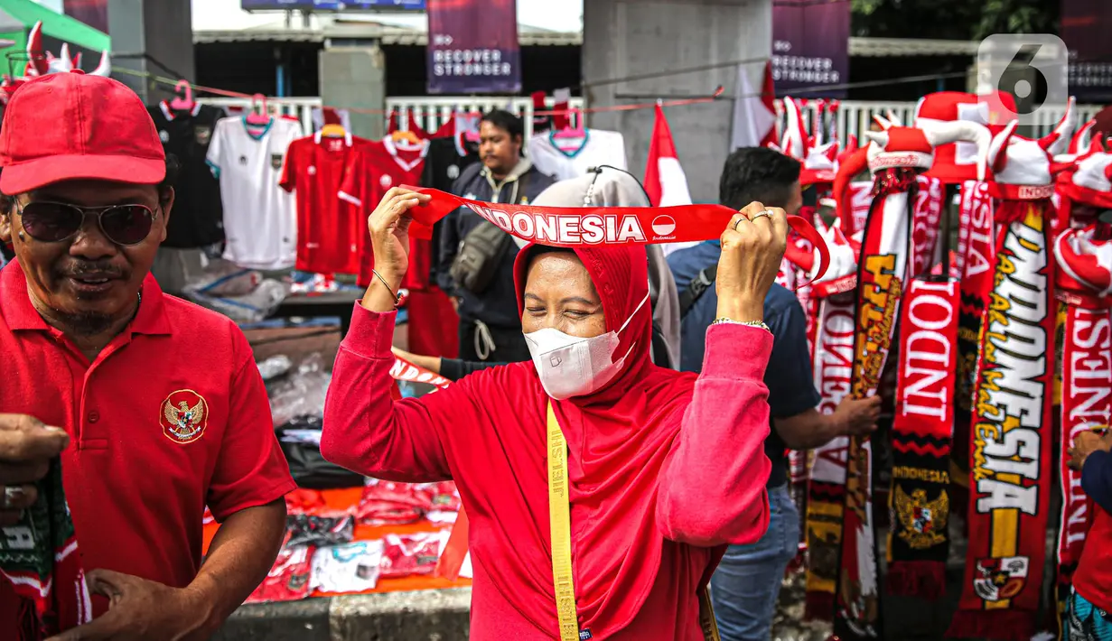 Seorang wanita mengenakan atribut Timnas Indonesia jelang pertandingan AFF 2022 antara Indonesia melawan Thailand di Stadion Gelora Bung Karno, Jakarta, Kamis (29/12/2022). Atribut timnas Indonesia seperti kaos, syal, dan topi dijual dengan kisaran harga Rp35.000 hingga Rp75.000. (Liputan6.com/Faizal Fanani)