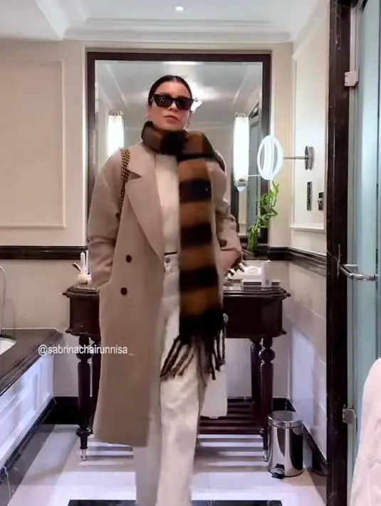 Tampil kece, Sabrina kali ini memadukan long coat warna khaki dengan knit top warna krem dan high waist pants warna putih. Dilengkapi syal dan kacamata hitam. @sabrinachairunnisa_/@mastercorbuzier.