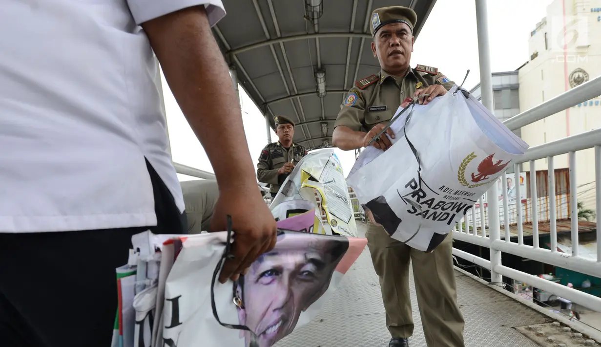Petugas Satpol PP membawa APK Pemilu 2019 di Kawasan Jalan Pemuda, Jakarta, Rabu (13/3). APK Pemilu 2019 yang terpasang pada JPO dibersihkan hal tersebut mengganggu dan melanggar aturan pemasangan dari komisi Pemilihan umum. (merdeka.com/Imam Buhori)