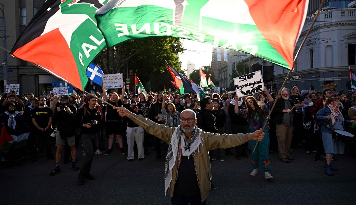 Para pengunjuk rasa mengibarkan bendera dan membawa plakat saat mereka berunjuk rasa selama kunjungan Presiden Israel, Isaac Herzog, di Melbourne, Australia, pada Kamis 12 Februari 2026. Ribuan orang menggelar aksi unjuk rasa di Melbourne, Australia. (WILLIAM WEST/AFP)