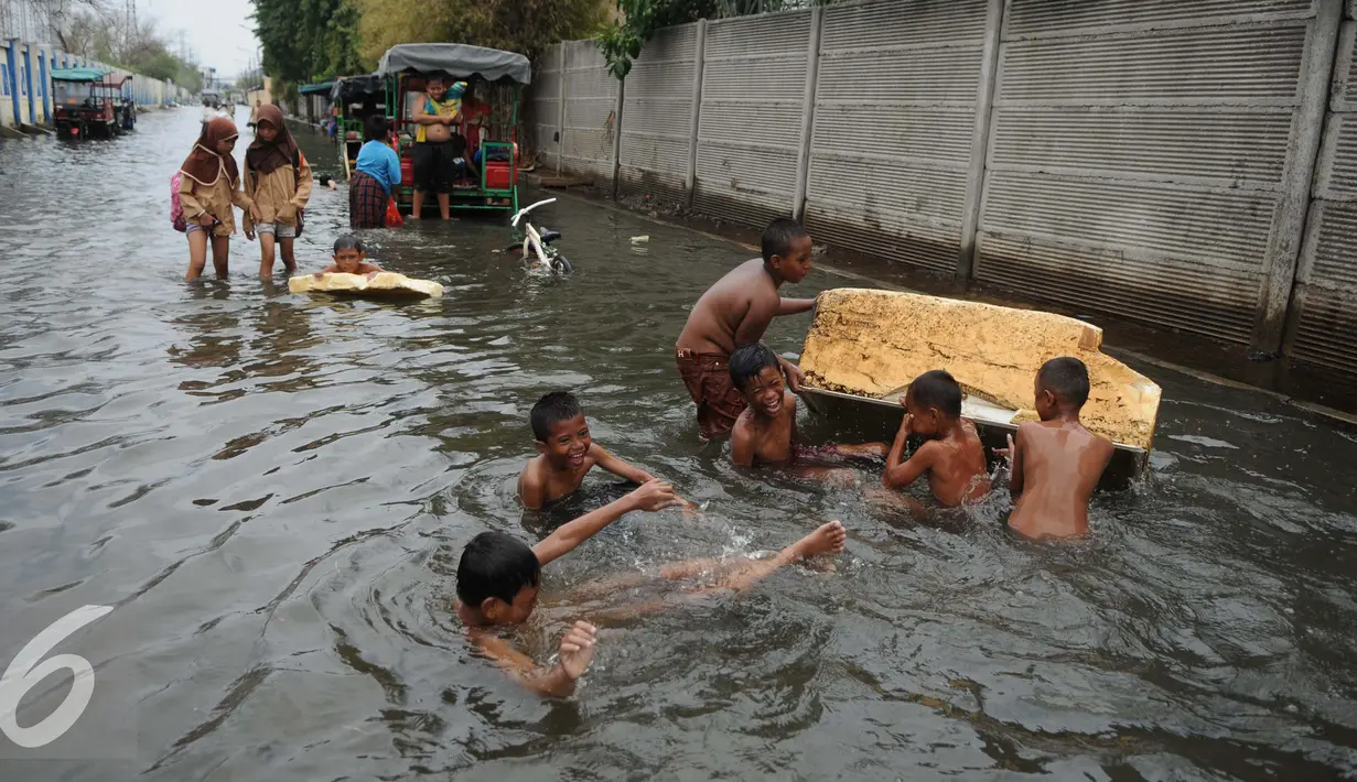 Sejumlah anak bermain di genangan air banjir di Kawasan Muara Angke, Jakarta, Rabu (11/1). Banjir ini juga telah merendam ratusan rumah, toko, dan tempat pengeringan ikan asin. (Liputan6.com/Gempur M. Surya)