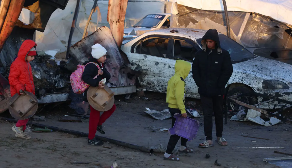 Anak-anak Palestina membawa barang-barang yang dapat diselamatkan berjalan di tengah kehancuran yang disebabkan oleh serangan Israel terhadap kamp pengungsian sementara di Mawasi Khan Yunis, Jalur Gaza selatan pada tanggal 2 Januari 2025. (BASHAR TALEB/AFP)