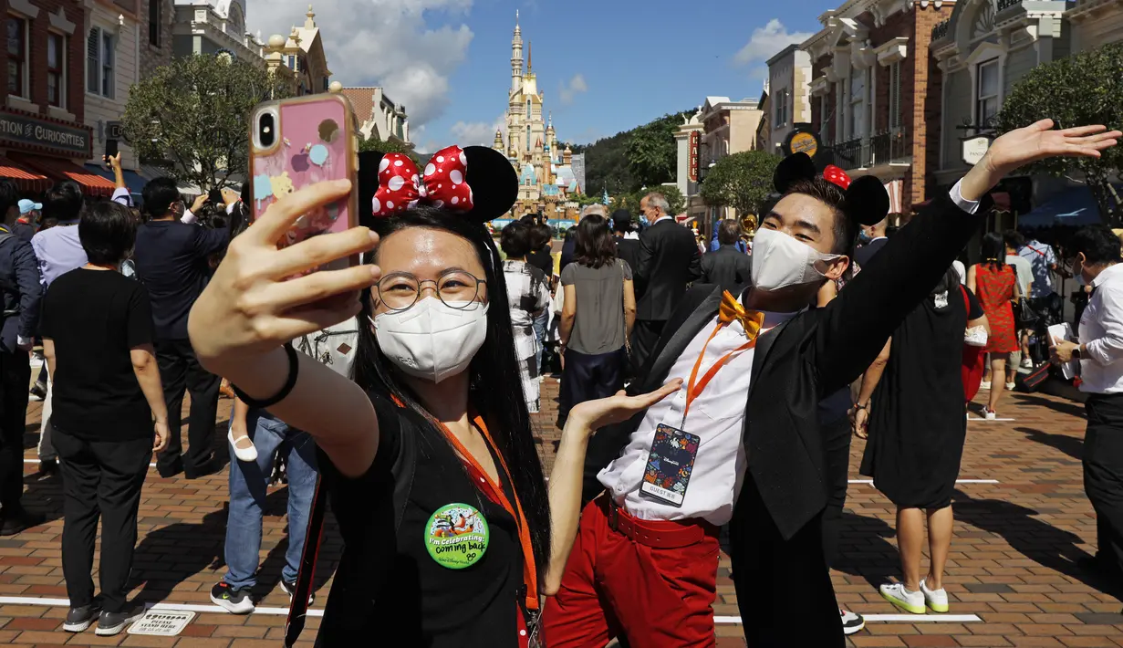 Disneyland Hong Kong Kembali Dibuka: Para pengunjung yang mengenakan masker untuk mencegah penyebaran COVID-19 berswafoto di Disneyland Hong Kong, Kamis (18/6/2020). Disneyland Hong Kong kembali beroperasi pada 18 Juni 2020 dengan menerapkan sejumlah protokol kesehatan baru. (AP Photo/Kin Cheung)