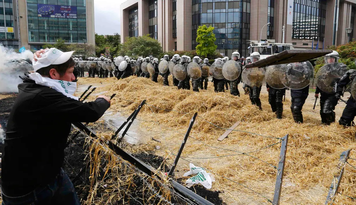 Sejumlah polisi berjaga saat peternak dan petani melempari jerami ditengah aksi protes pada pertemuan Menteri-menteri Eropoa di Brussels, Belgia, 7 September 2015. Aksi tersebut menuntut bantuan harga murah dan biaya yang tinggi. REUTERS/Yves Herman)