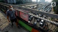 Pejalan kaki yang mengenakan masker berjalan di atas jembatan penyeberangan orang (JPO) dengan arus lalu lintas yang macet di kawasan Jalan TB Simatupang, Jakarta, Rabu (15/8/2023). Kementerian Lingkungan Hidup dan Kehutanan (KLHK) menilai, sumber pencemaran kualitas udara alias polusi udara Jakarta dan sekitarnya masih didominasi oleh sektor transportasi. (merdeka.com/Arie Basuki)