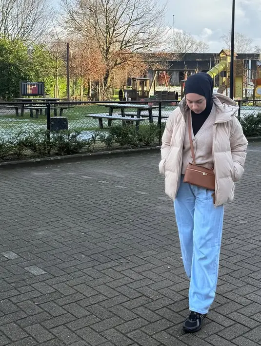 Irish kembali mengenakan kerudung polos hitam, dipadukan sweater ivory yang senada dengan luaran jaket paddingnya. Ia memilih mengenakan sling bag coklat dari Loro Piana dan celana denim panjang.  [@_irishbella_]