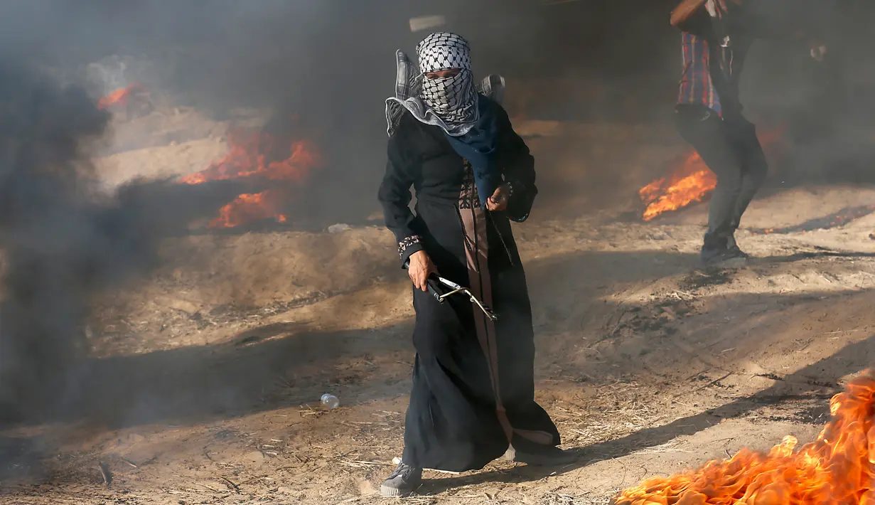<p>Pengunjuk rasa wanita Palestina memegang ketapel di tengah asap hitam saat terjadi bentrok antara warga dengan tentara Israel di Khan Younis, perbatasan Gaza, Jumat (10/8). (AP Photo/Adel Hana)</p>