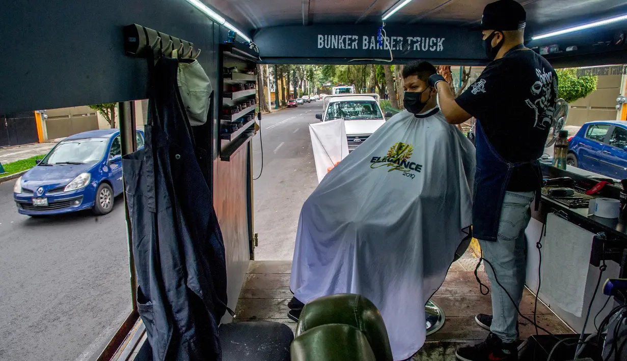 Seorang tukang cukur memotong rambut pelanggan di mobil van atau truck yang diubah menjadi barbershop di sebuah jalan di tengah pandemi virus corona COVID-19, di Mexico City, pada Minggu (6/9/2020). (Photo by CLAUDIO CRUZ / AFP)