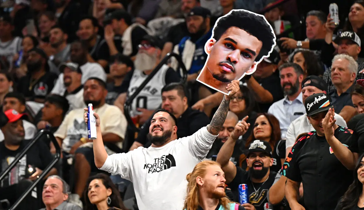 Seorang penonton membawa poster berbentuk muka pebasket San Antonio Spurs, Victor Wembanyama pada laga NBA musim 2023/2024 melawan Dallas Mavericks di AT&T Center in San Antonio, Texas, Kamis (27/10/2023). (AFP/Chandan Khanna)